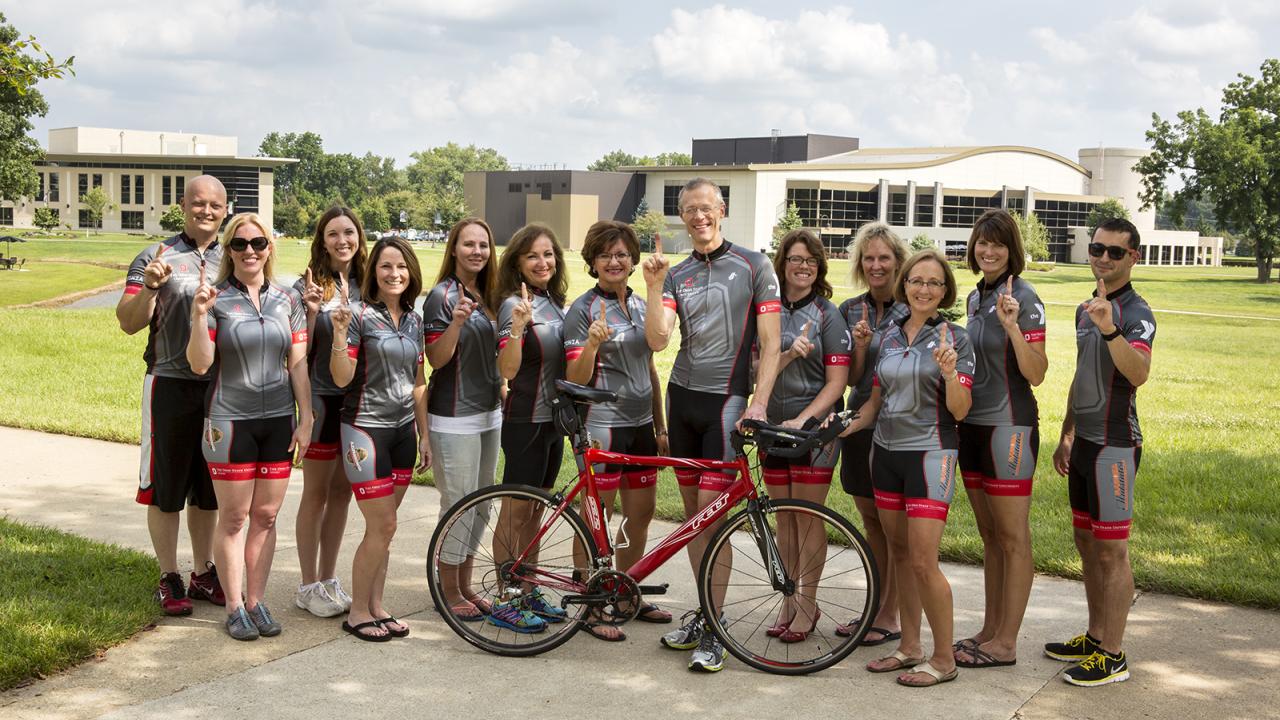 Thirteen member of Team Buckeye - Rolling for a Cure stand behind a bicycle on the Newark campus.