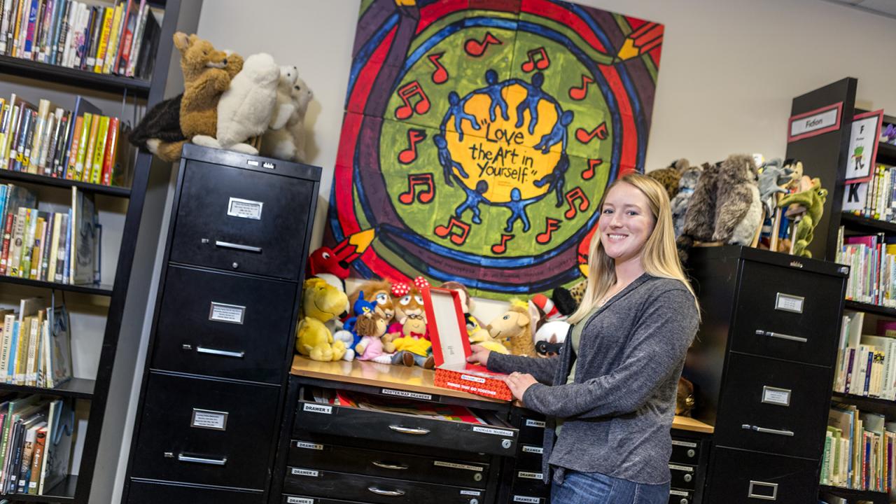 A student stands at a cabinet with children's books and plush animals.