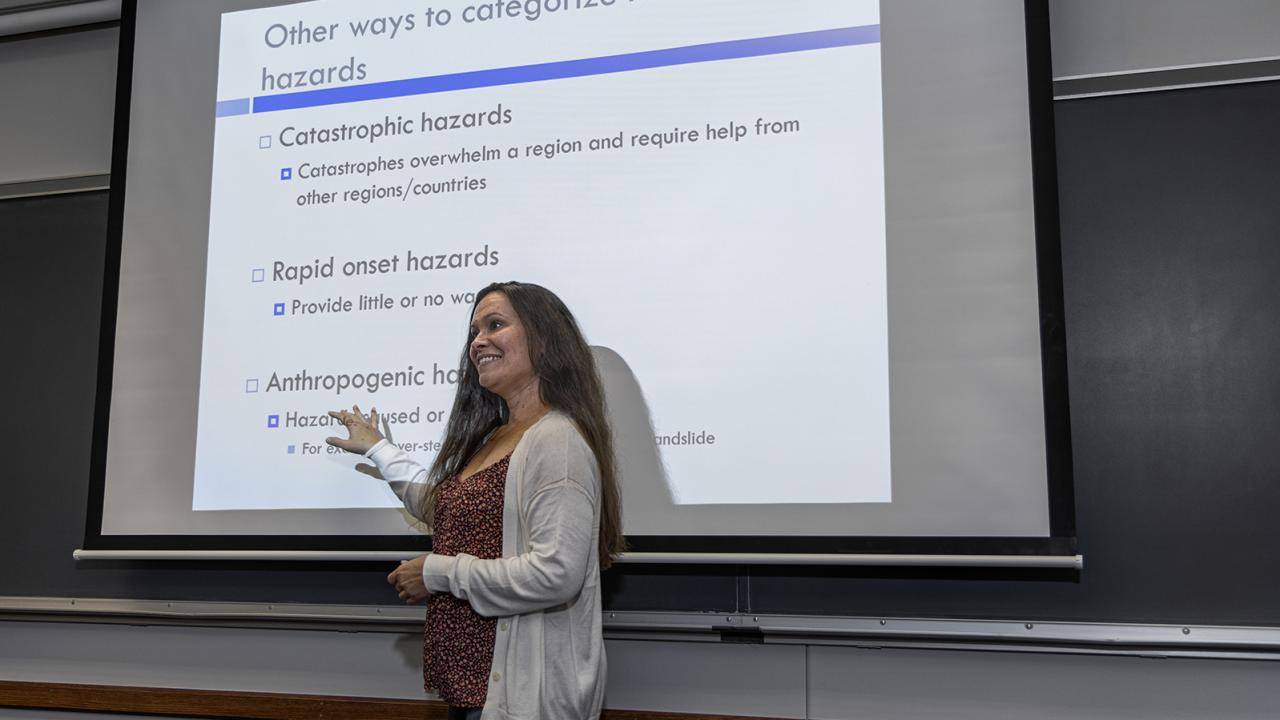 A faculty member stands in front of a screen with a lesson projected onto it. 