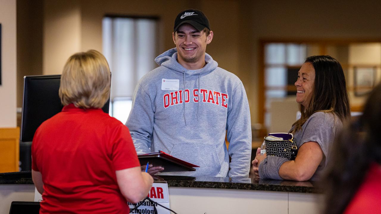 A male student with his mom next to him speak with a staff member at orientation.