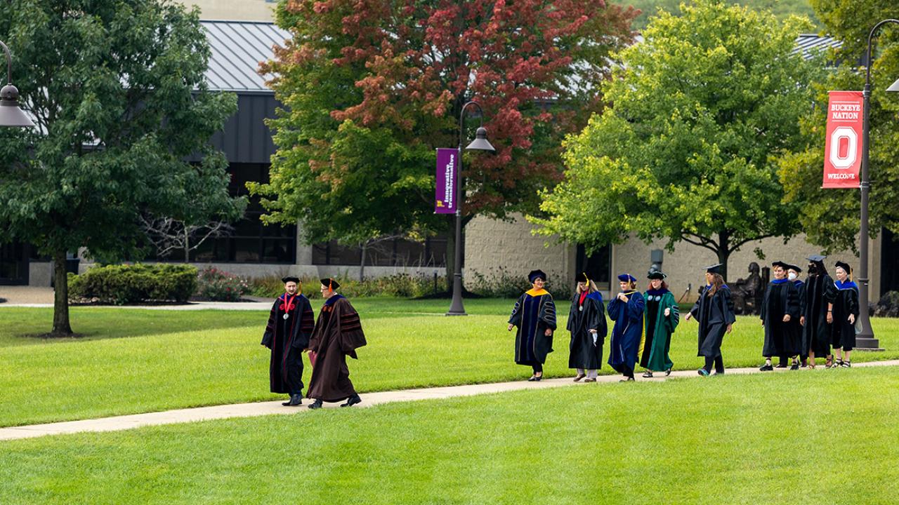 Members of the academic administration walk across campus wearing academic regalia during Convocation.