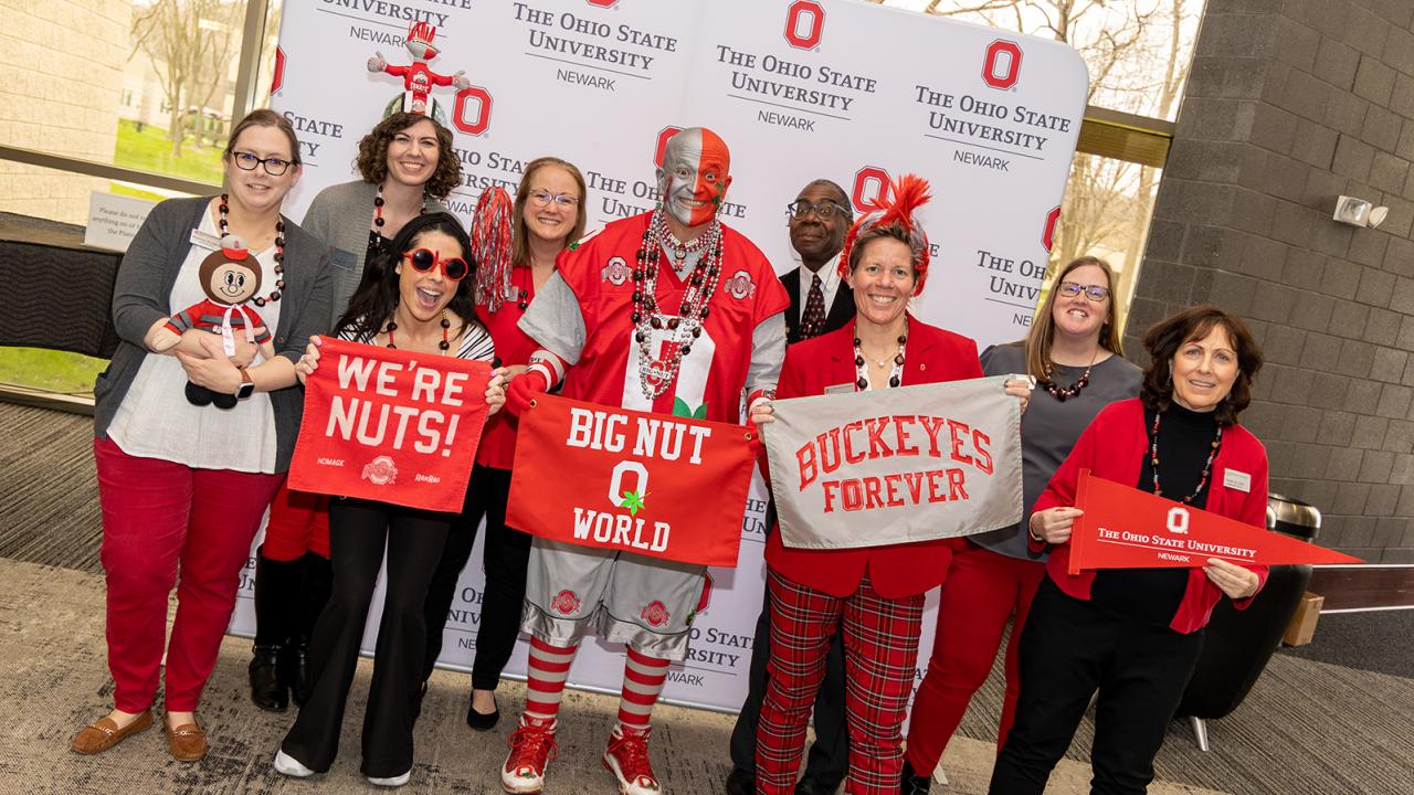 Member of the admissions office staff surround Buckeye fan Big Nut wearing their buckeye spirit wear and holding Buckeye paraphernalia .