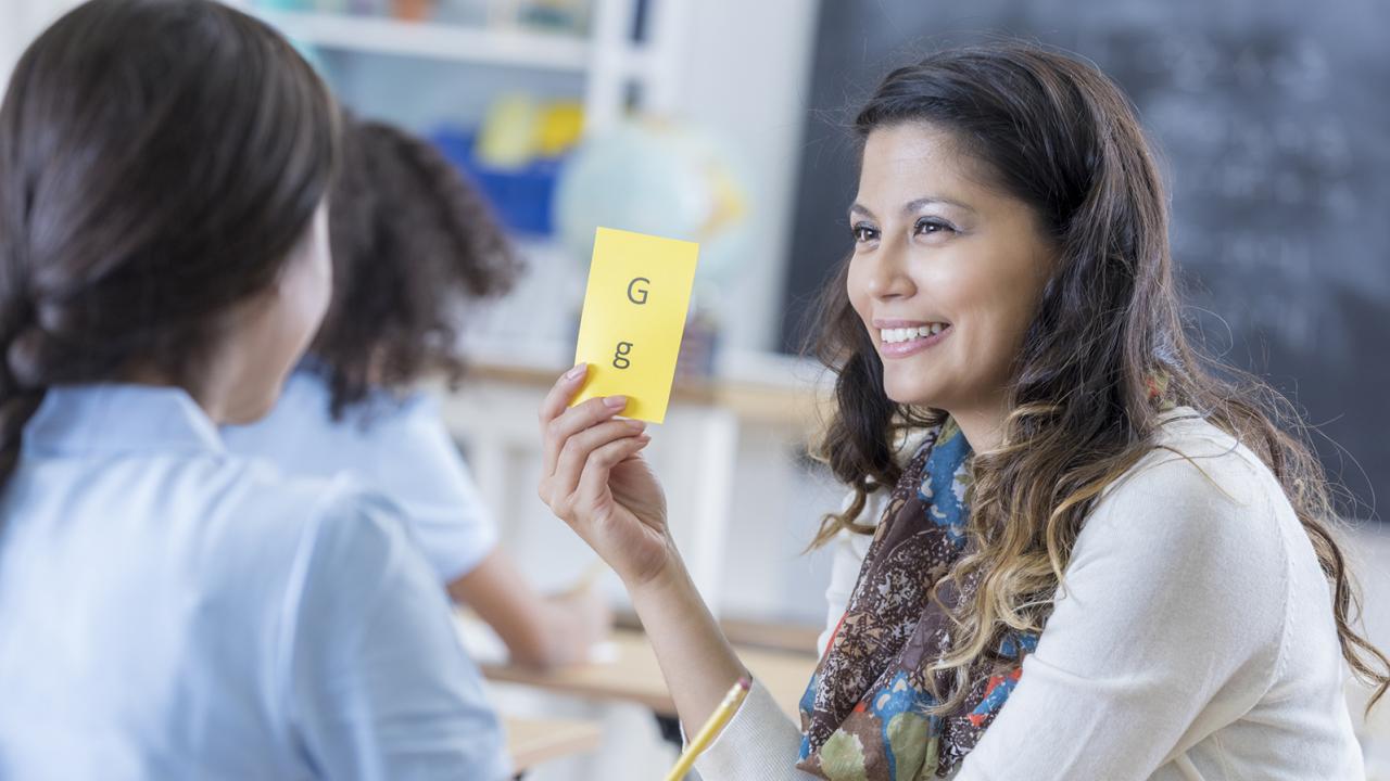 A teacher holds up a flash card with letters in front of a student.