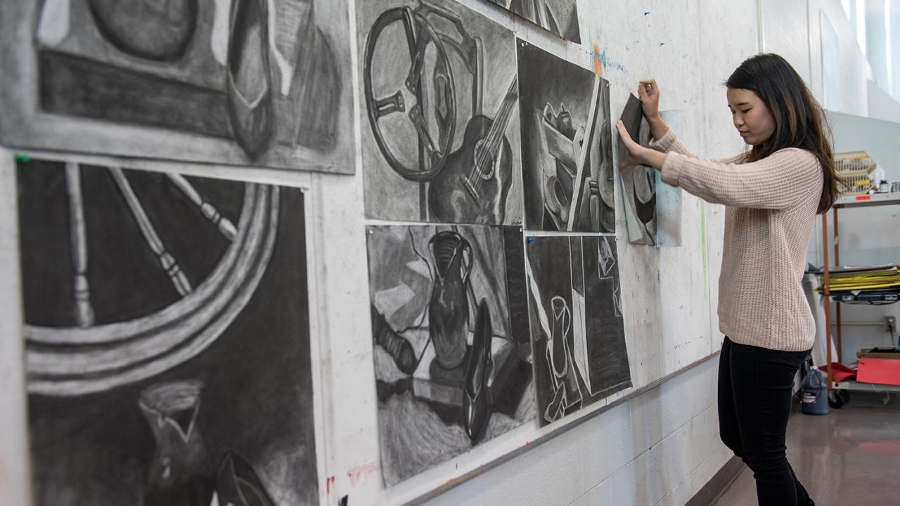 A student hangs her drawing along a wall of other students' drawings. 