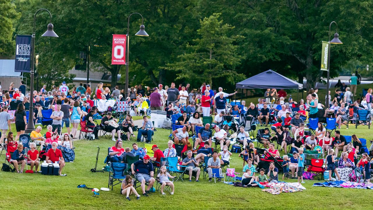 People of all ages gather on the campus lawn in chairs, under tents, and on blankets to enjoy a concert and fireworks.