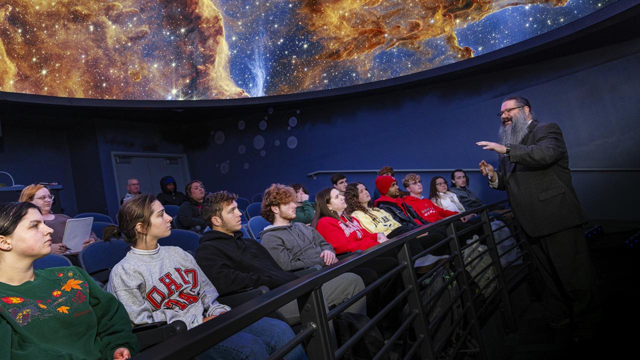 Michael Stamatikos stands at the front of a class in the SciDome planetarium. 