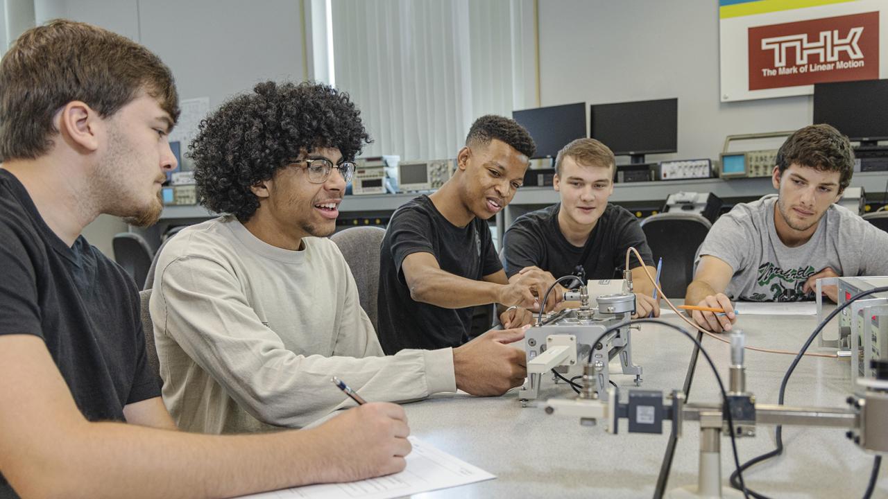 A group of students sitting around a table interact with electrical equipment on it.