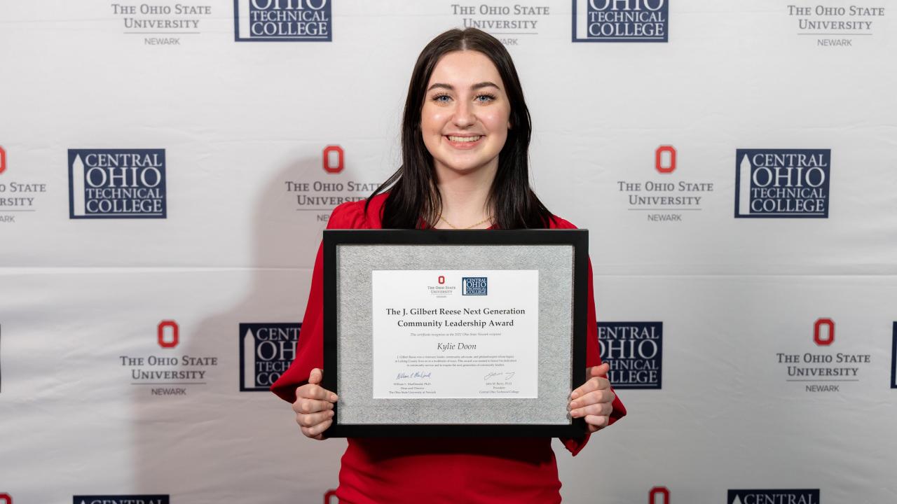 Portrait of Kylie Doon holding a framed award certificate.