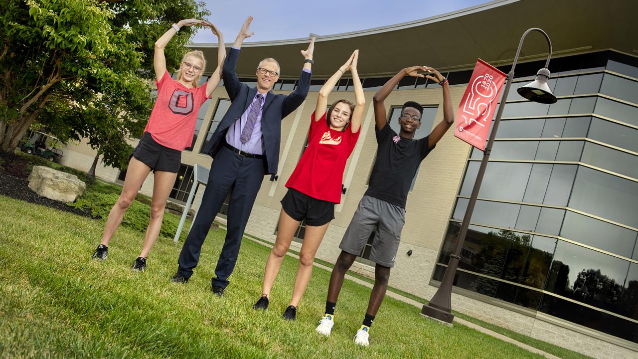 Dean William MacDonald and three students form the letters O, H, I and O with their arms. 