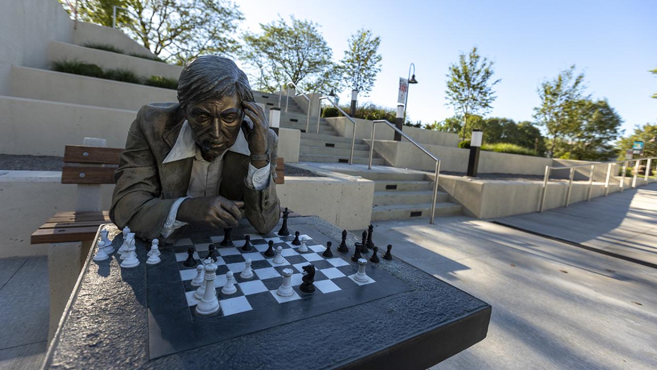 A statue of a man playing chess at an outdoor table.