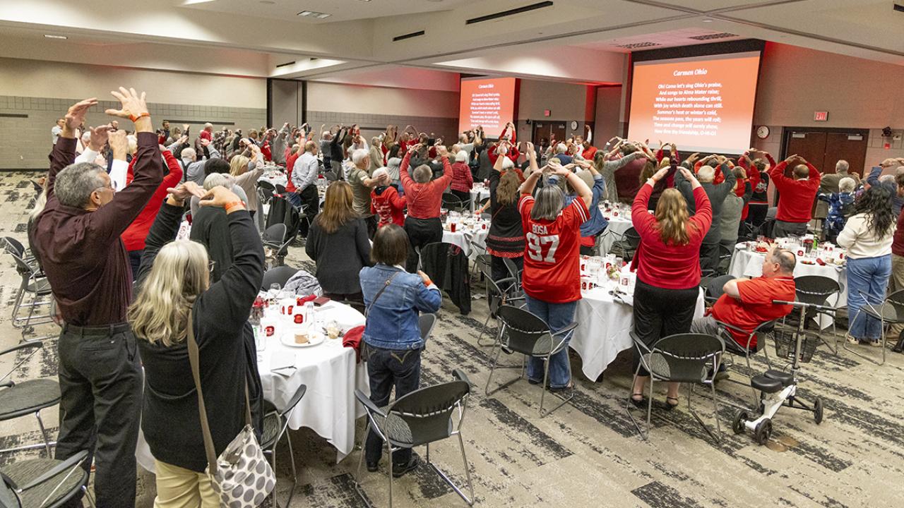 Attendees raise their arms above their heads in an O formation.