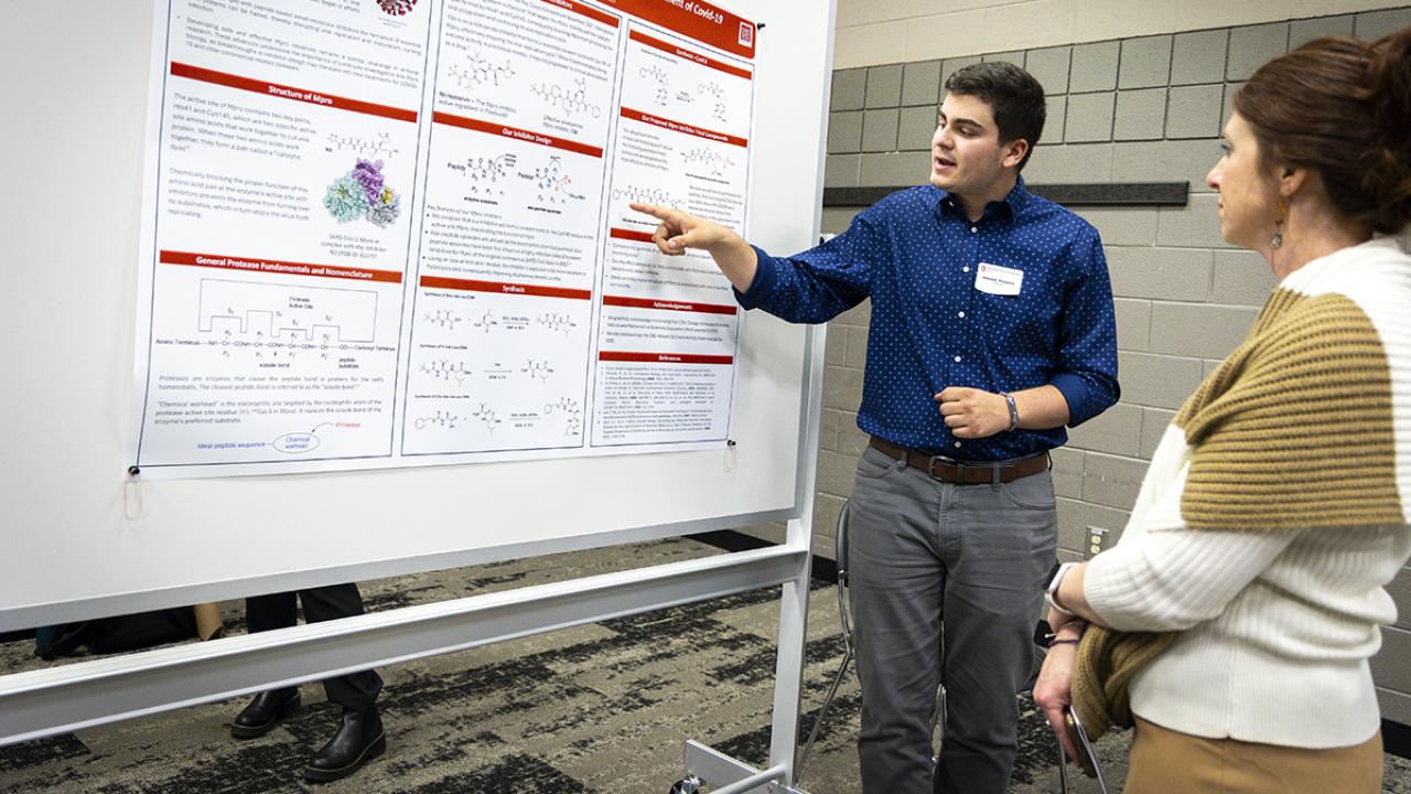 A student points to his research poster during a presentation at the Student Research and Scholarship Forum.