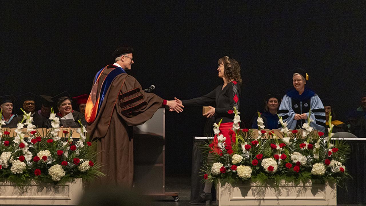 Dean William MacDonald and a graduating student extend their arms to shake hands on the stage.