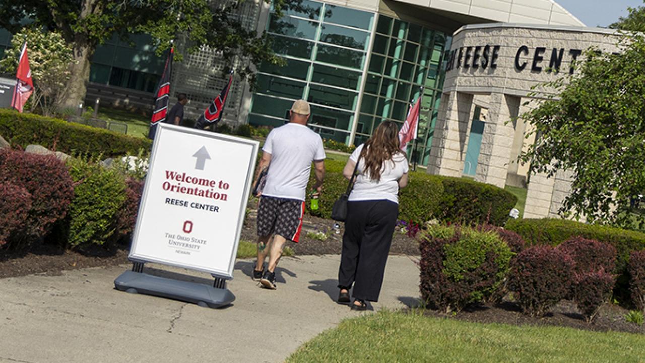 Two people walk past a sign that says "Welcome to orientation" outside of the Reese Center on campus.
