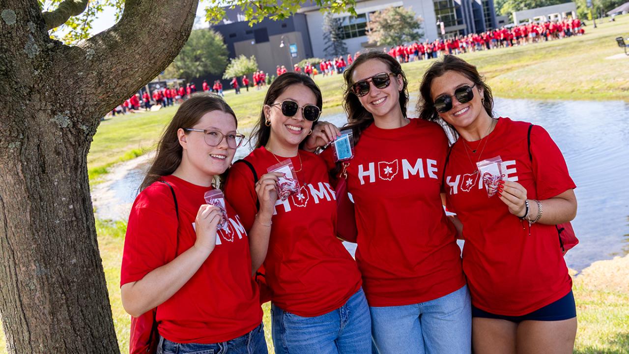 Four students stand together holding up their scarlet and gray tassels they just received as part of the Convocation tradition.