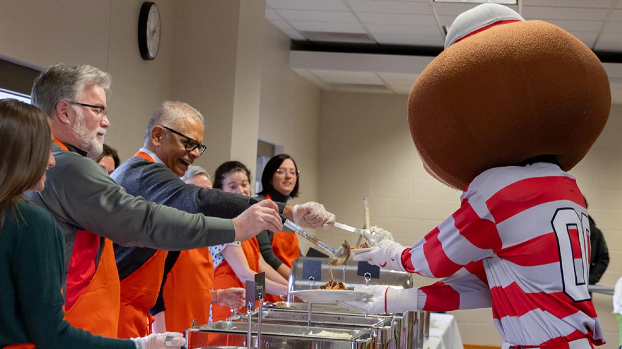 Brutus Buckeye goes through a buffet line and is served food by faculty and staff.