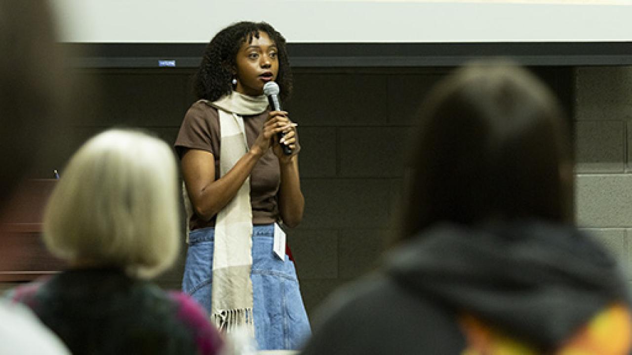 Student Mikiah Fant stands in front of an audience speaking into a microphone during the oral presentations of the Student Research and Creative Inquiry Forum.